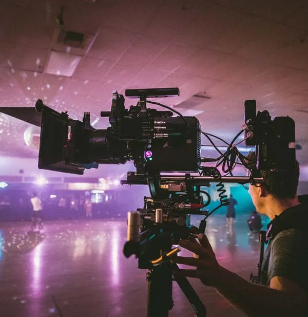 Person operating a professional video camera in an indoor setting with dim lighting and a disco ball hanging from the ceiling.