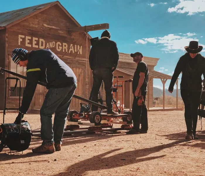 Film crew setting up equipment in front of a Western-style 