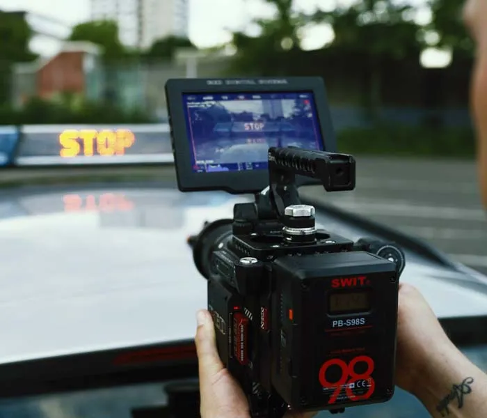 A person operates a professional video camera mounted on a vehicle, with 