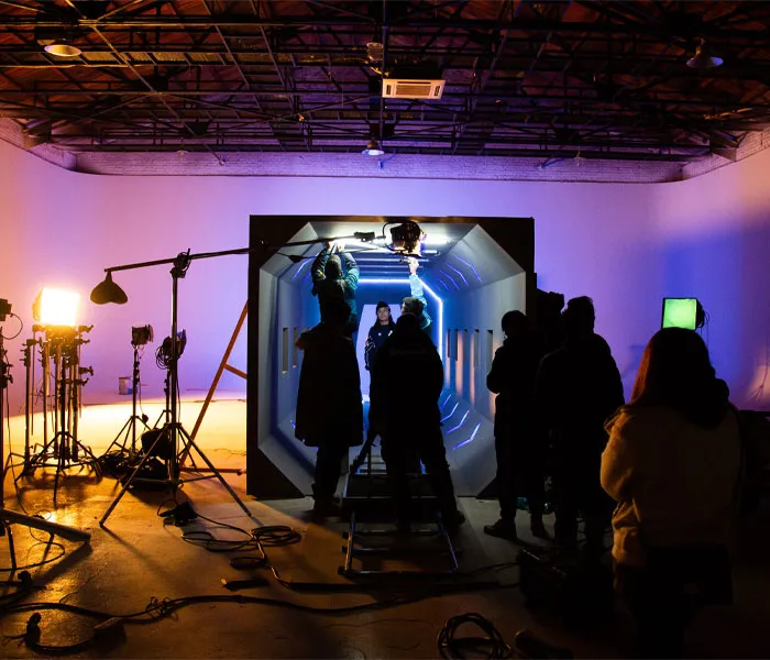 Film crew on set in a studio, gathering around a sci-fi themed tunnel set with various lighting and filming equipment.