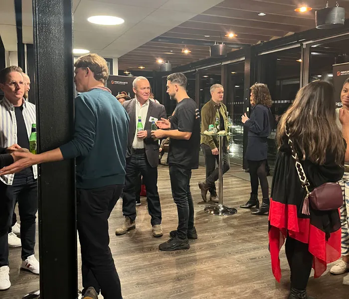 A group of people standing and talking in a well-lit indoor area with drinks in hand, attending a social gathering.