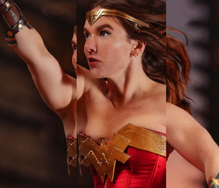 A woman dressed as Wonder Woman poses with her arm raised, wearing a red and gold costume with a headpiece while looking determined.