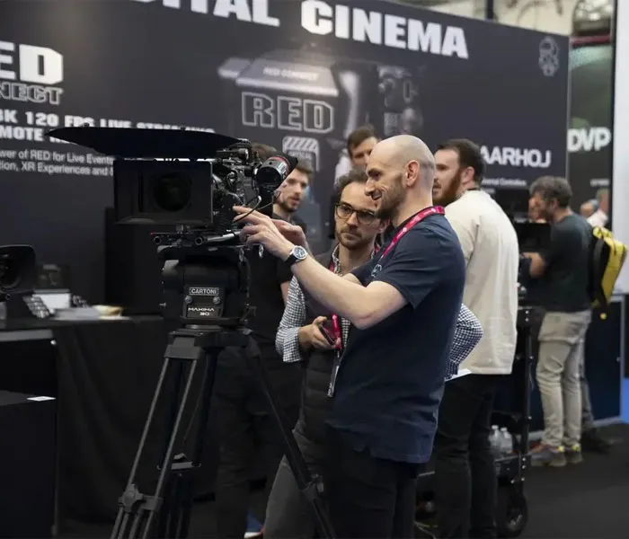 People examining a professional camera setup at an exhibition booth, with 