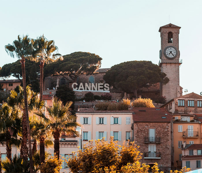 A view of Cannes with a prominent clock tower and a hillside sign reading 