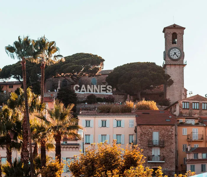 A view of Cannes with a prominent clock tower and a hillside sign reading 