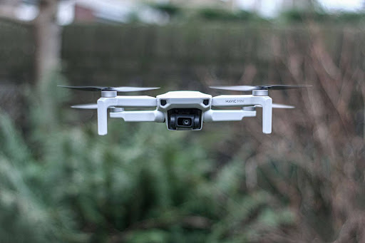 A white drone hovers above a vibrant garden, capturing the beauty of the flowers and greenery below.