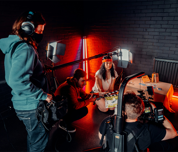 Film crew setting up a scene with a female actor in costume, surrounded by professional lighting and camera equipment.