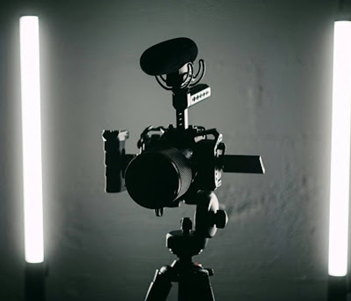 A camera with a microphone is mounted on a tripod, flanked by two vertical light bars in a dimly lit setting.