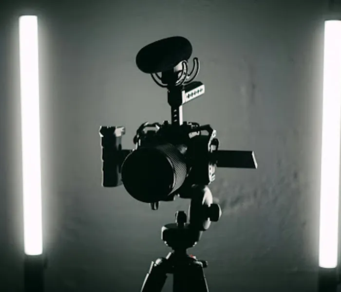 A camera with a microphone is mounted on a tripod, flanked by two vertical light bars in a dimly lit setting.