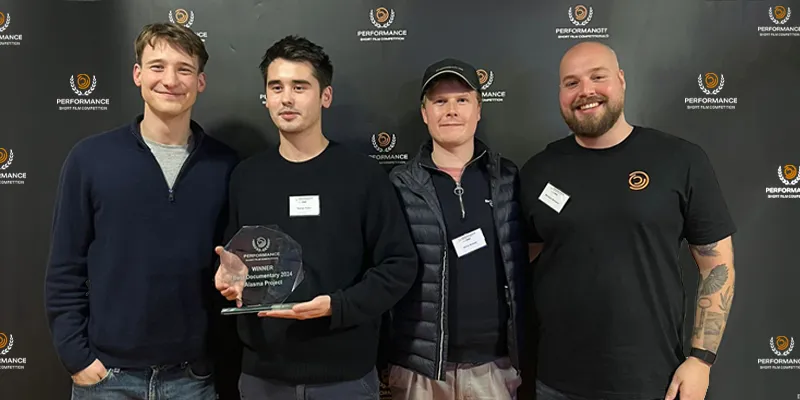 Four people stand together in front of a backdrop, with one holding an award.