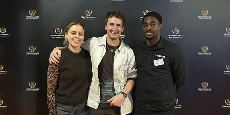 Three people smiling and posing with an award plaque in front of a black backdrop with logos.