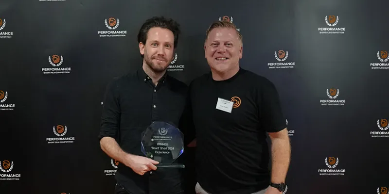 Two people standing in front of a branded backdrop, one holding an award labeled "Winner Best Start 2022.