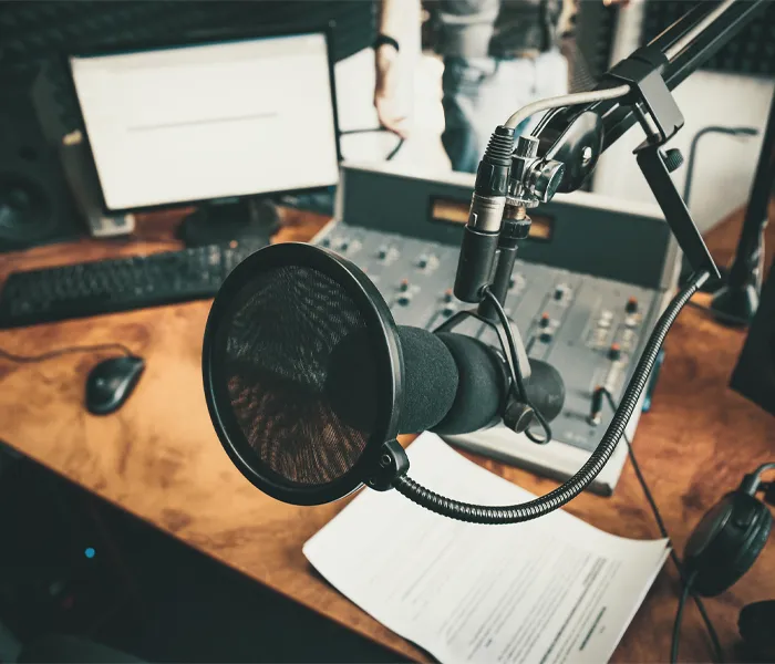 Close-up of a podcast or radio station setup with a microphone, mixer, and computer on a wooden desk.